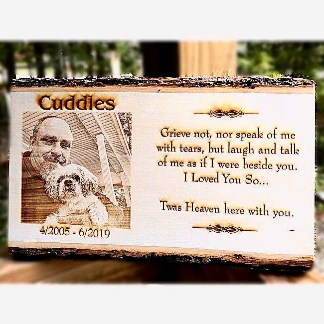 Memorial plaque with engraved text and a photo of a man and a dog, set against a blurred natural background.