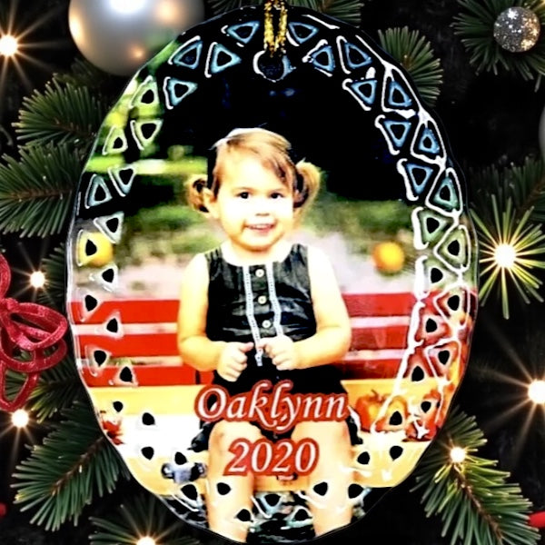 Christmas ornament with a photo of a child and 'Oaklynn 2020' text, surrounded by festive decorations.