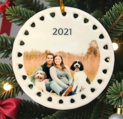 Round ornament with a photo of a couple and two dogs, dated 2021, hanging on a Christmas tree.