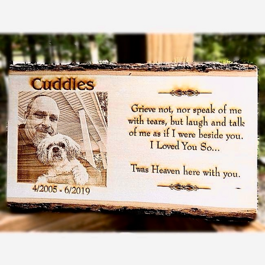 Memorial plaque with engraved text and a photo of a man and a dog, set against a blurred natural background.