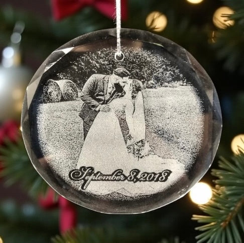 Decorative glass ornament with a engraved photo and date, hanging on a Christmas tree.